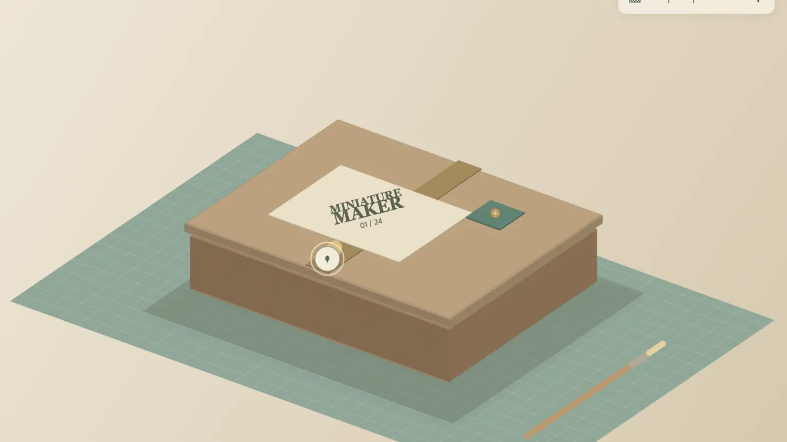 Miniature Maker: a closed brown box with a cream label on a green gridded cutting mat beside a paintbrush.